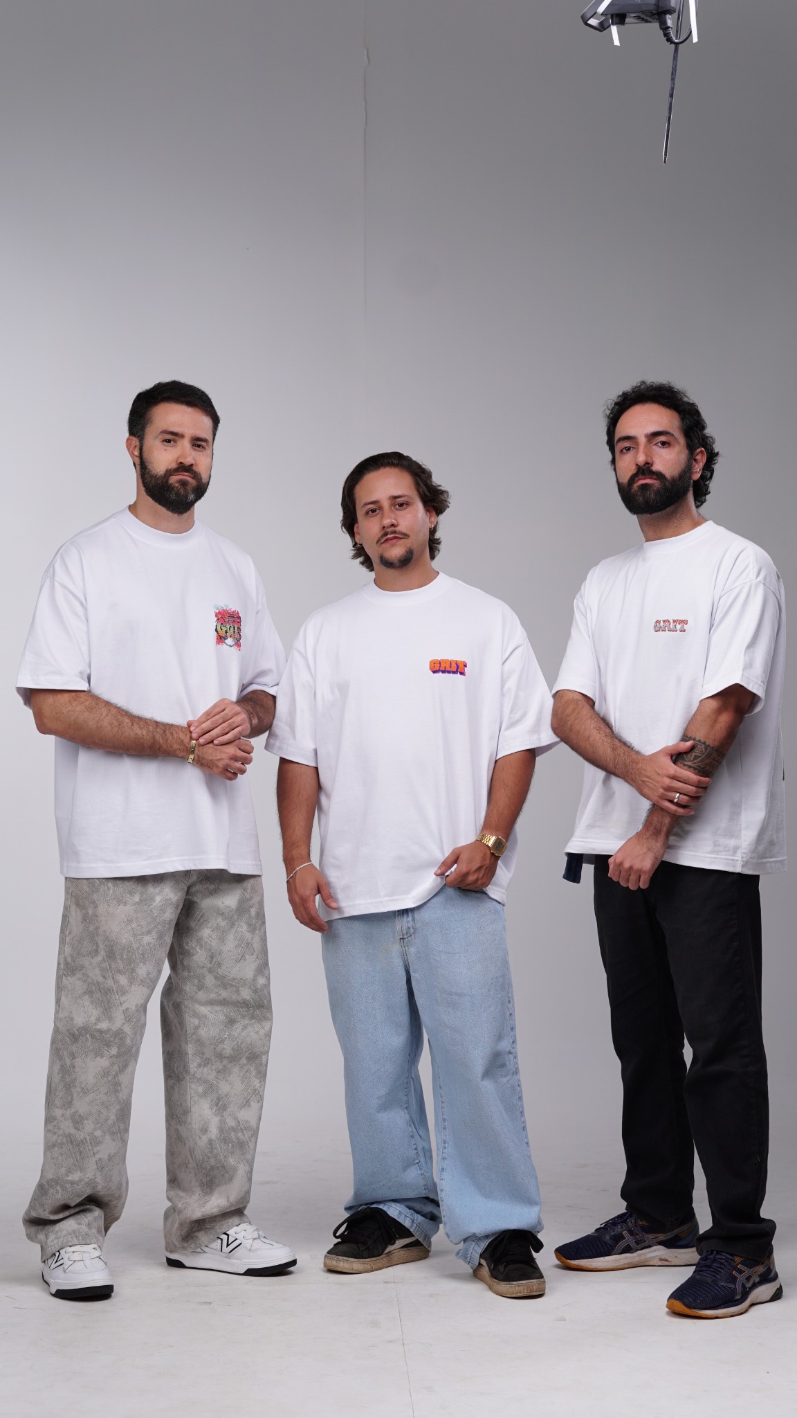 Fotografia completa dos três modelos da GRIT juntos, vestindo camisetas brancas, da cabeça aos pés